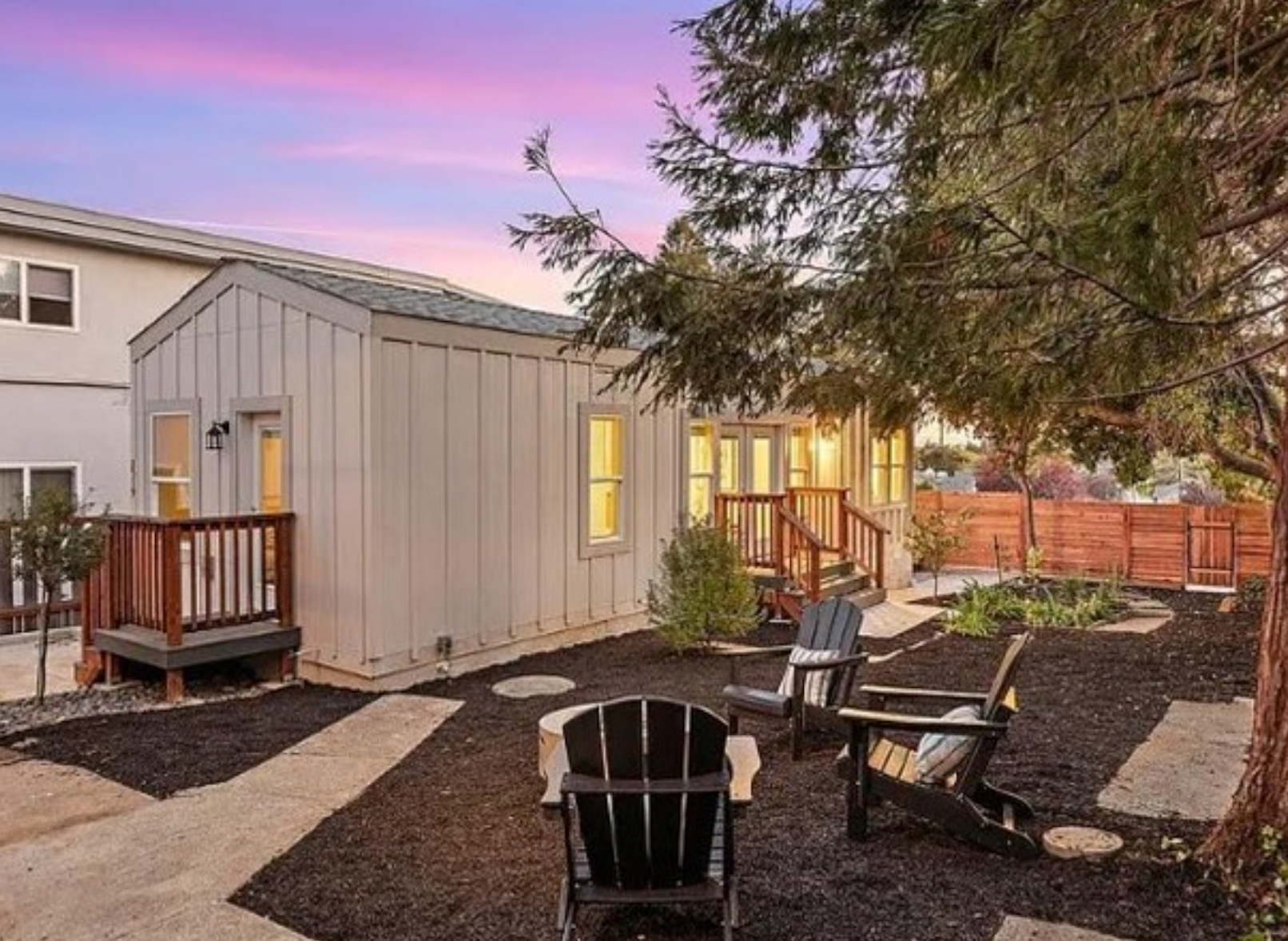 Perpetual Homes ADU: Backyard with chairs around a fire pit, small house, wooden deck, pink and blue sunset.