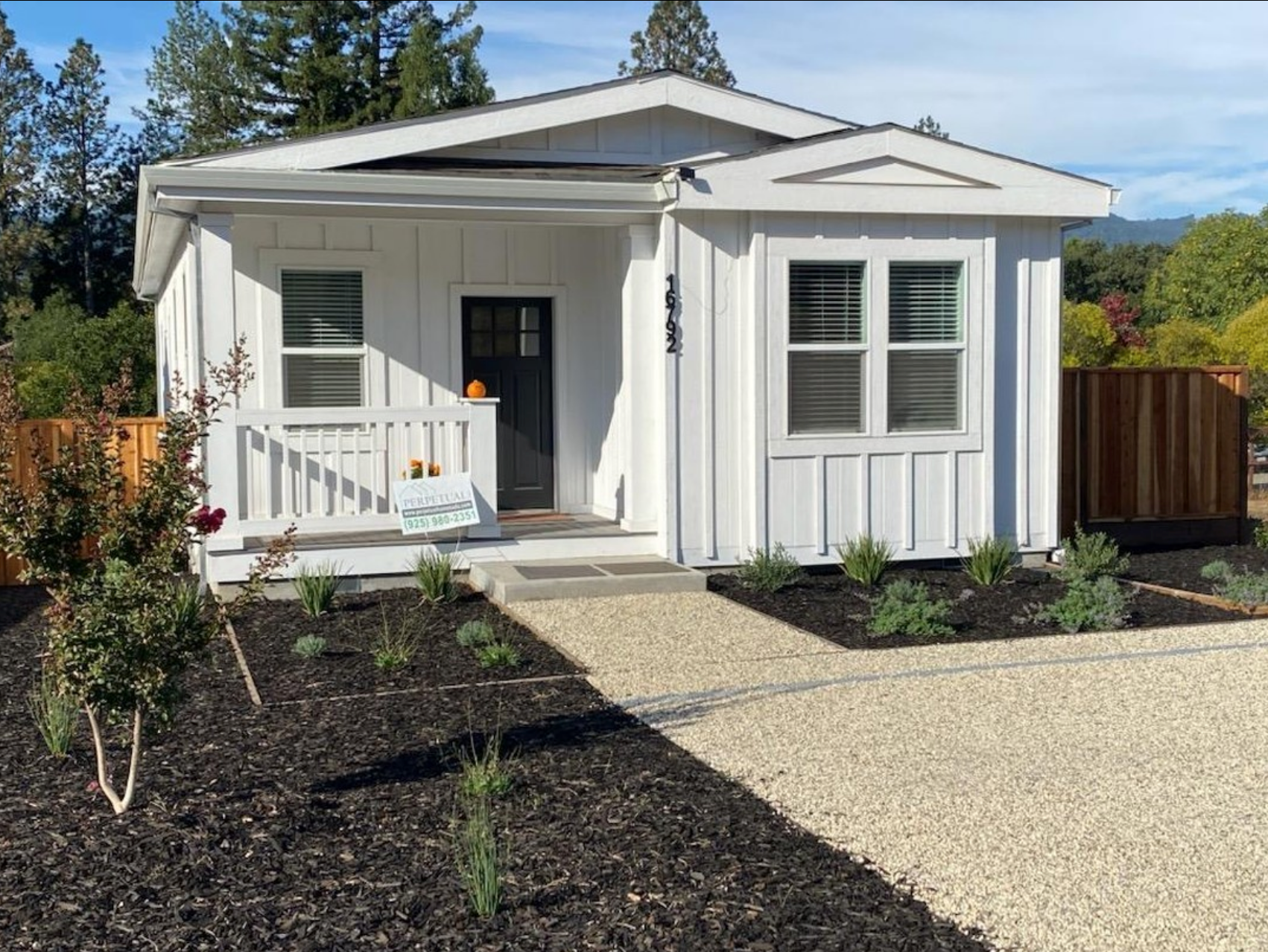 Perpetual Homes ADU: White-painted cottage with a black door, porch, and gravel walkway.