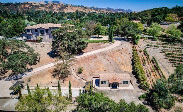 Perpetual Homes ADU: Two-story house and smaller cottage on a hillside with a vineyard and surrounding trees.