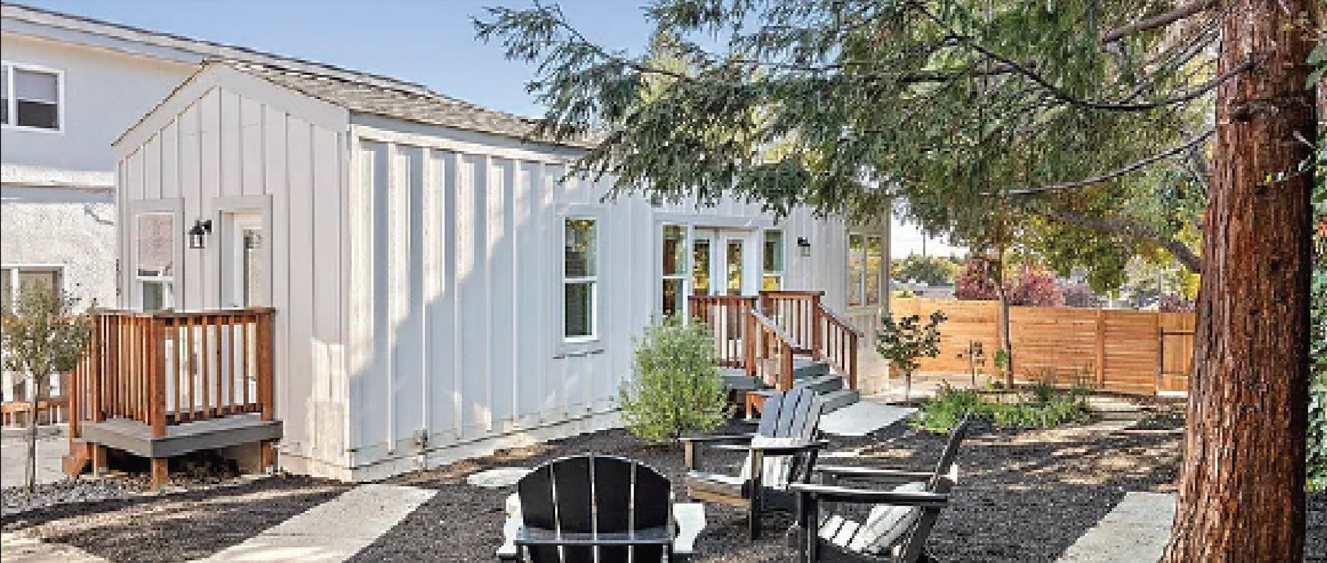 Perpetual Homes ADU: White backyard house with a small deck, patio furniture, and a tree.