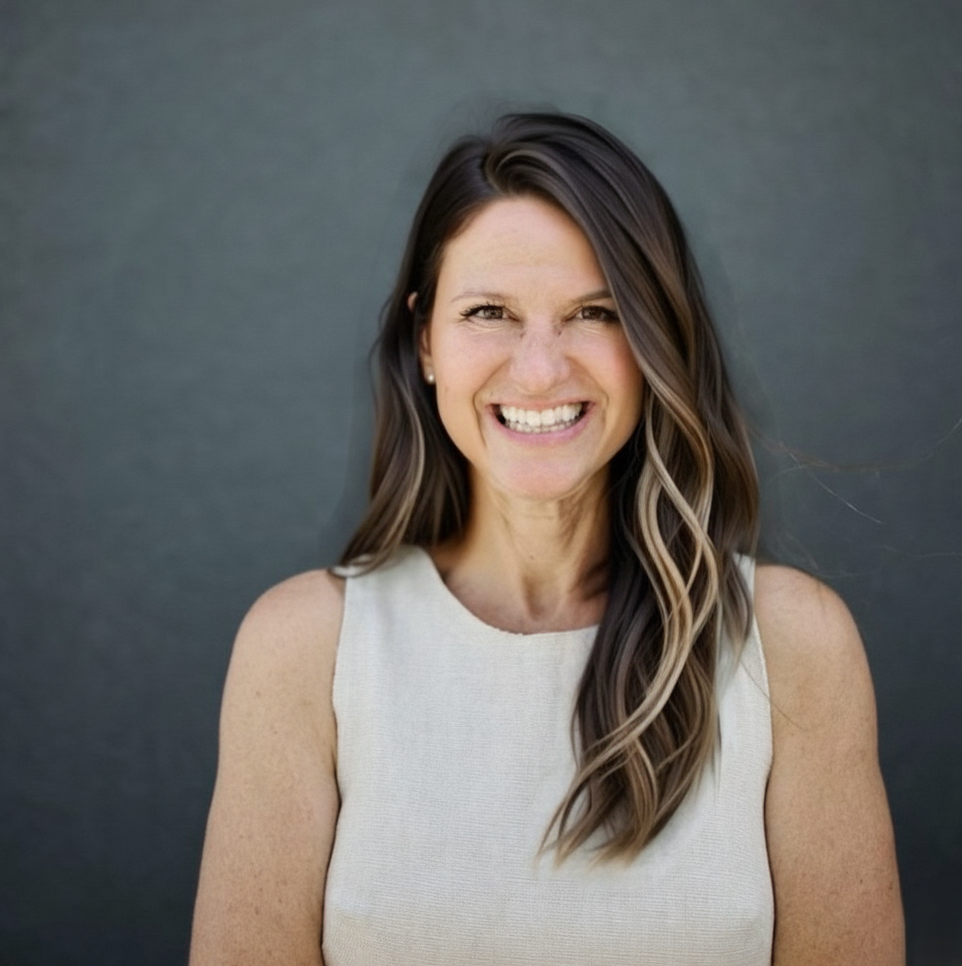 Trisha Guido, Perpetual Homes ADU. Woman smiling, leaning against a gray wall, wearing a sleeveless cream-colored top.