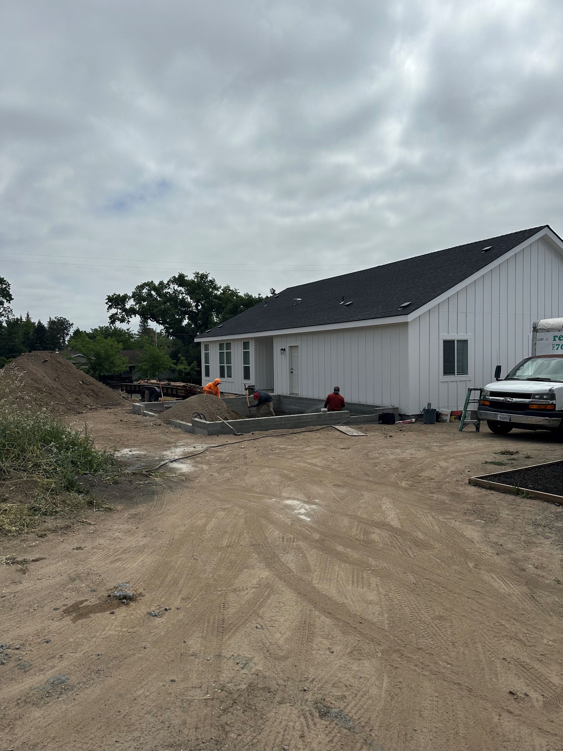 Perpetual Homes ADU: White building under construction with dirt driveway and pile of gravel, cloudy sky.