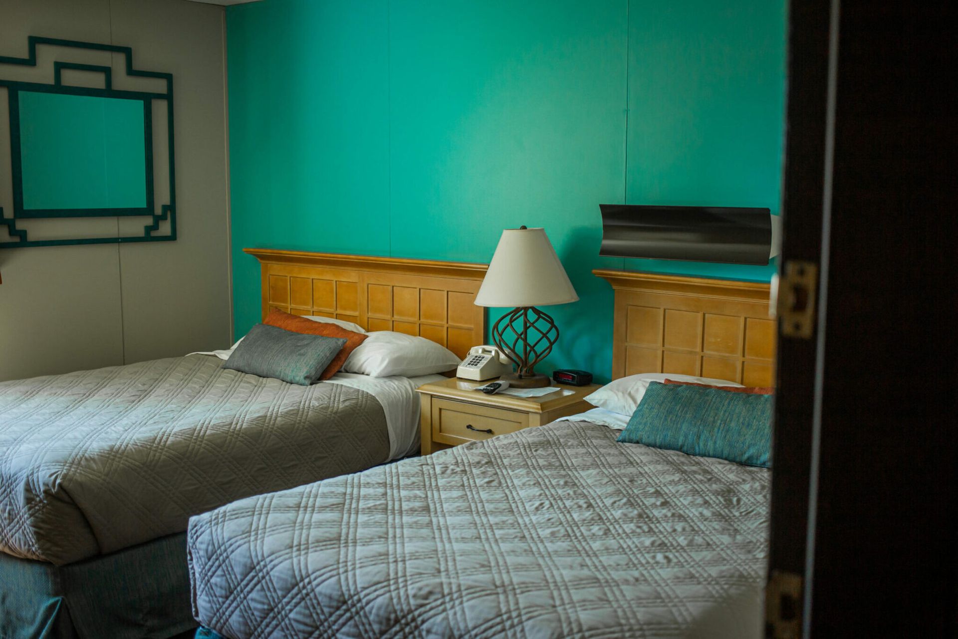 Tidy bedroom with two beds, teal walls, wood headboards, and a bedside lamp