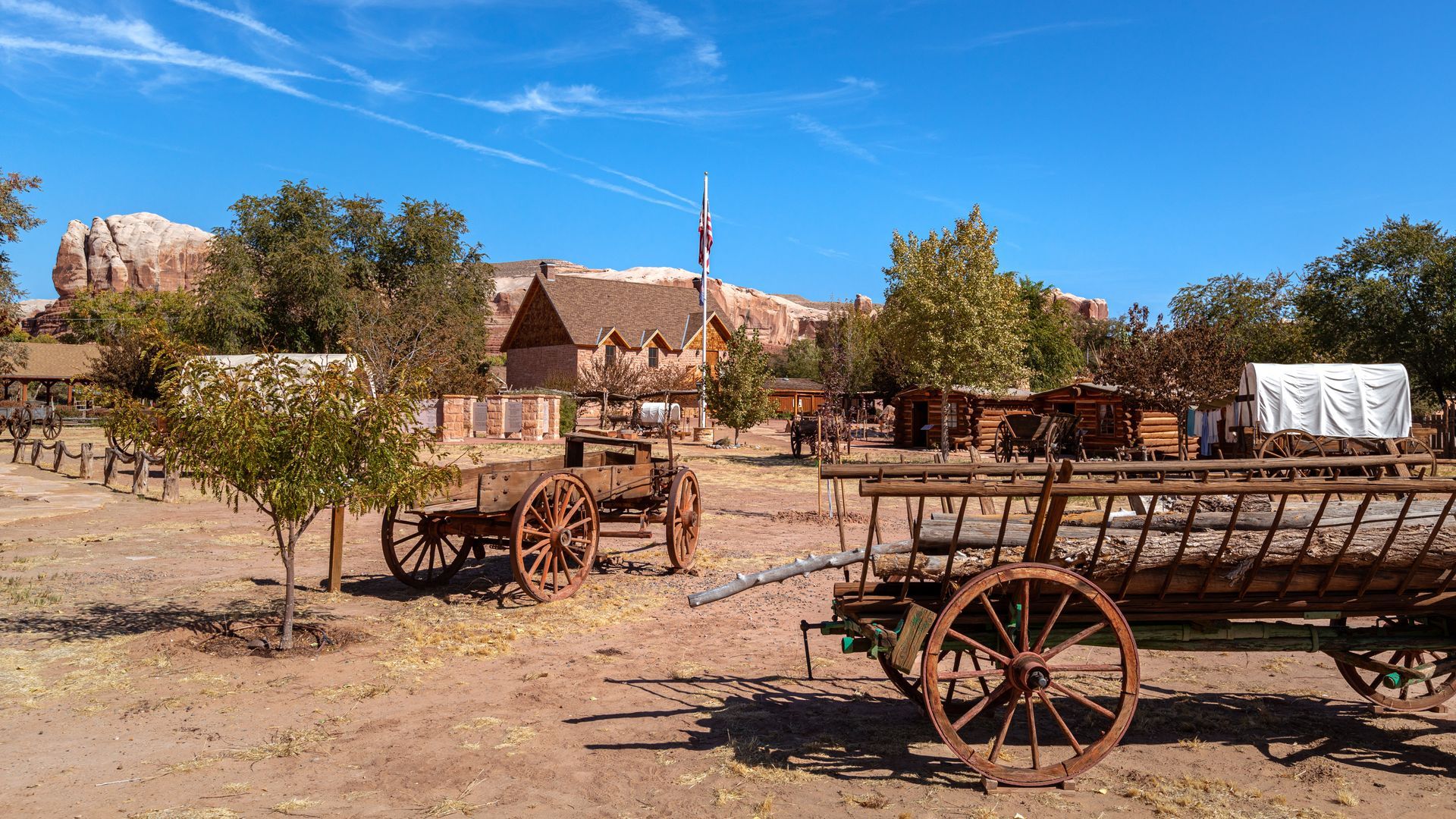 Old western town with wooden wagons, dirt ground, and rustic buildings under a clear blue sky