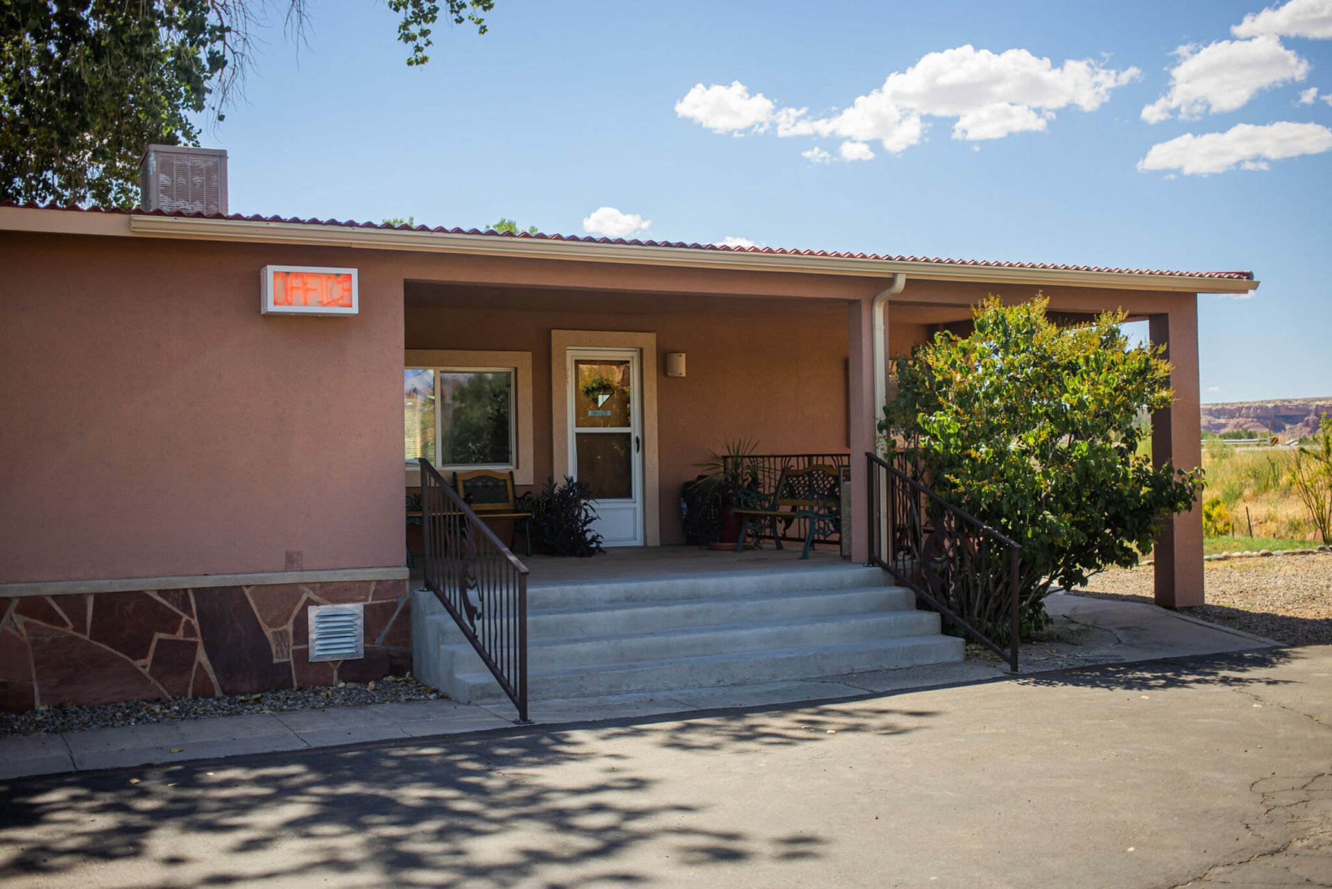 Small tan building with steps, ramp, and a front porch under a blue sky