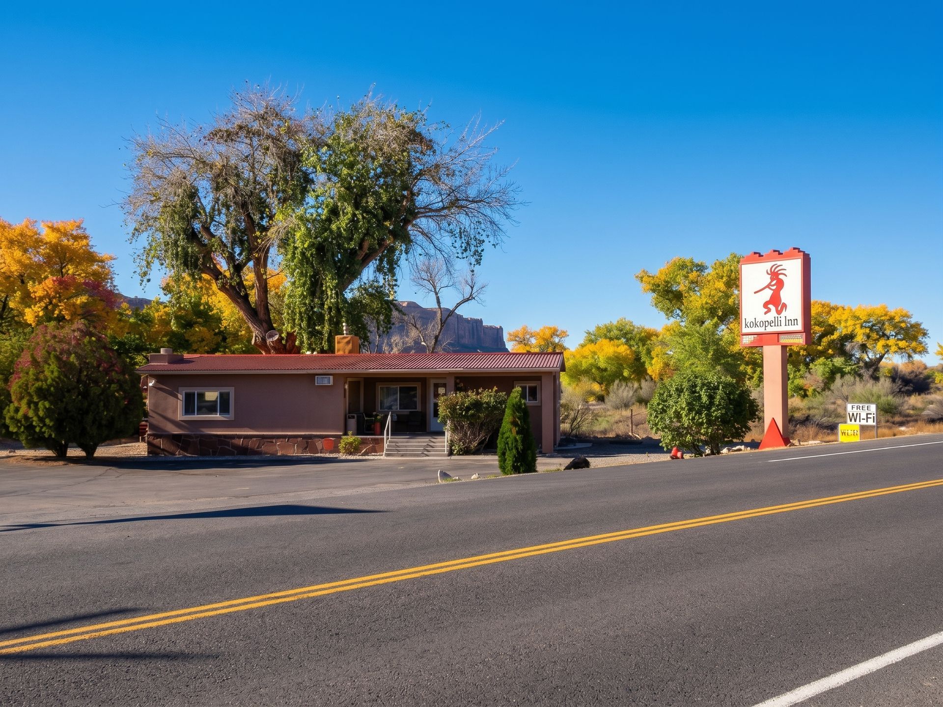 Roadside restaurant with a red sign, autumn trees, and a blue sky along a paved highway.
