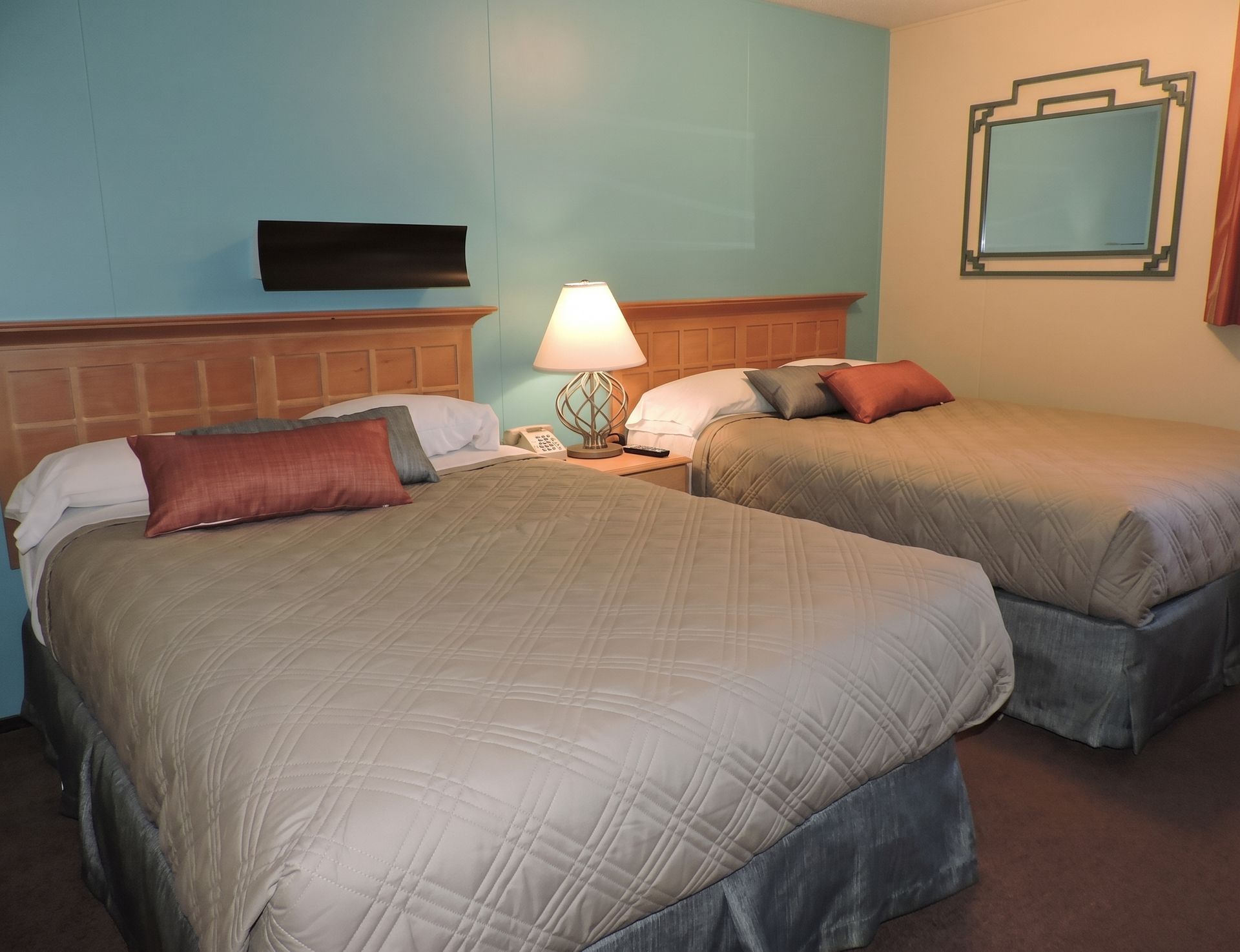 Hotel room with two beds, a bedside lamp, and a wall mirror in soft blue and beige tones