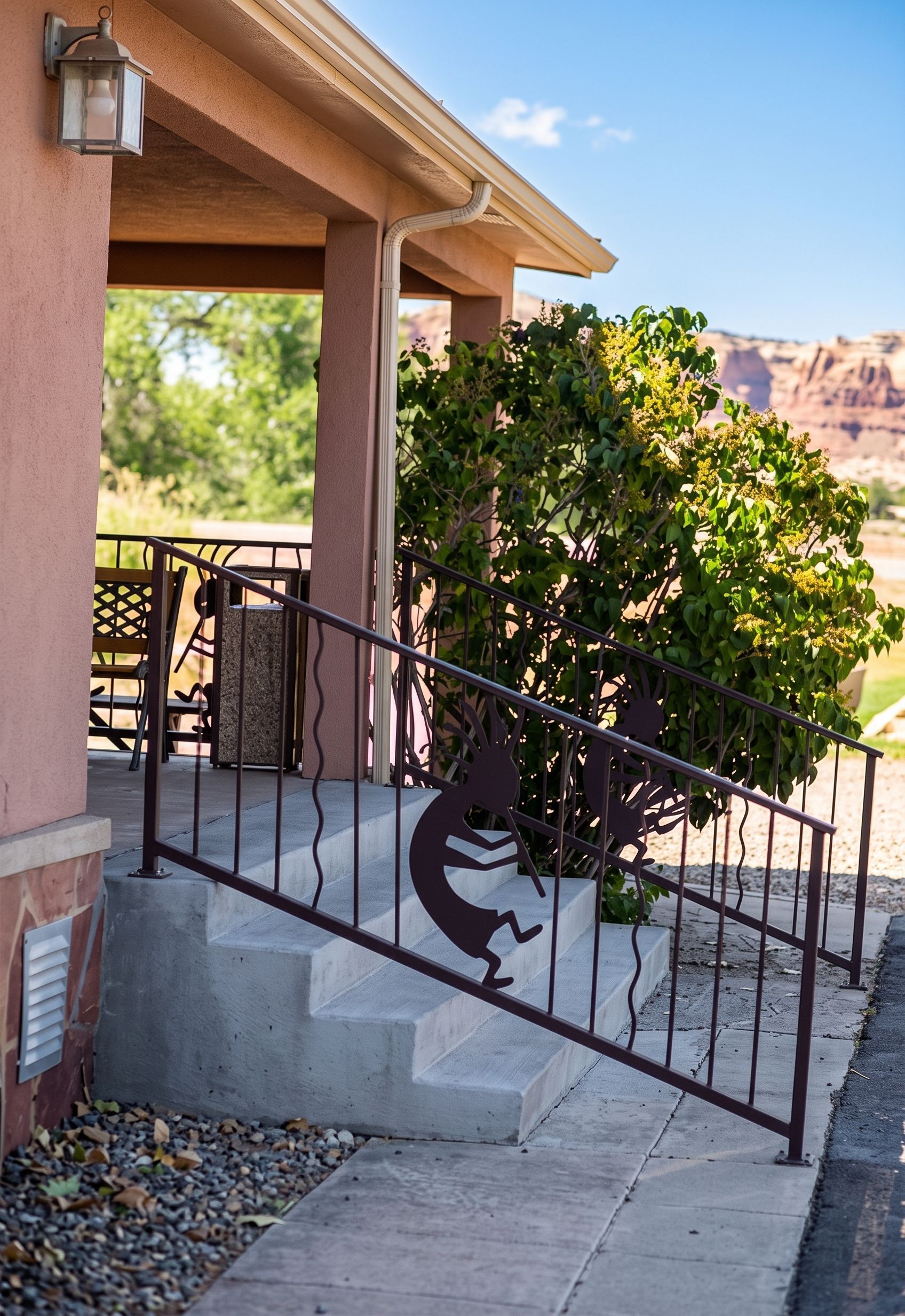 Desert house porch with stairs, black railing, and a large leafy plant in a sunny yard