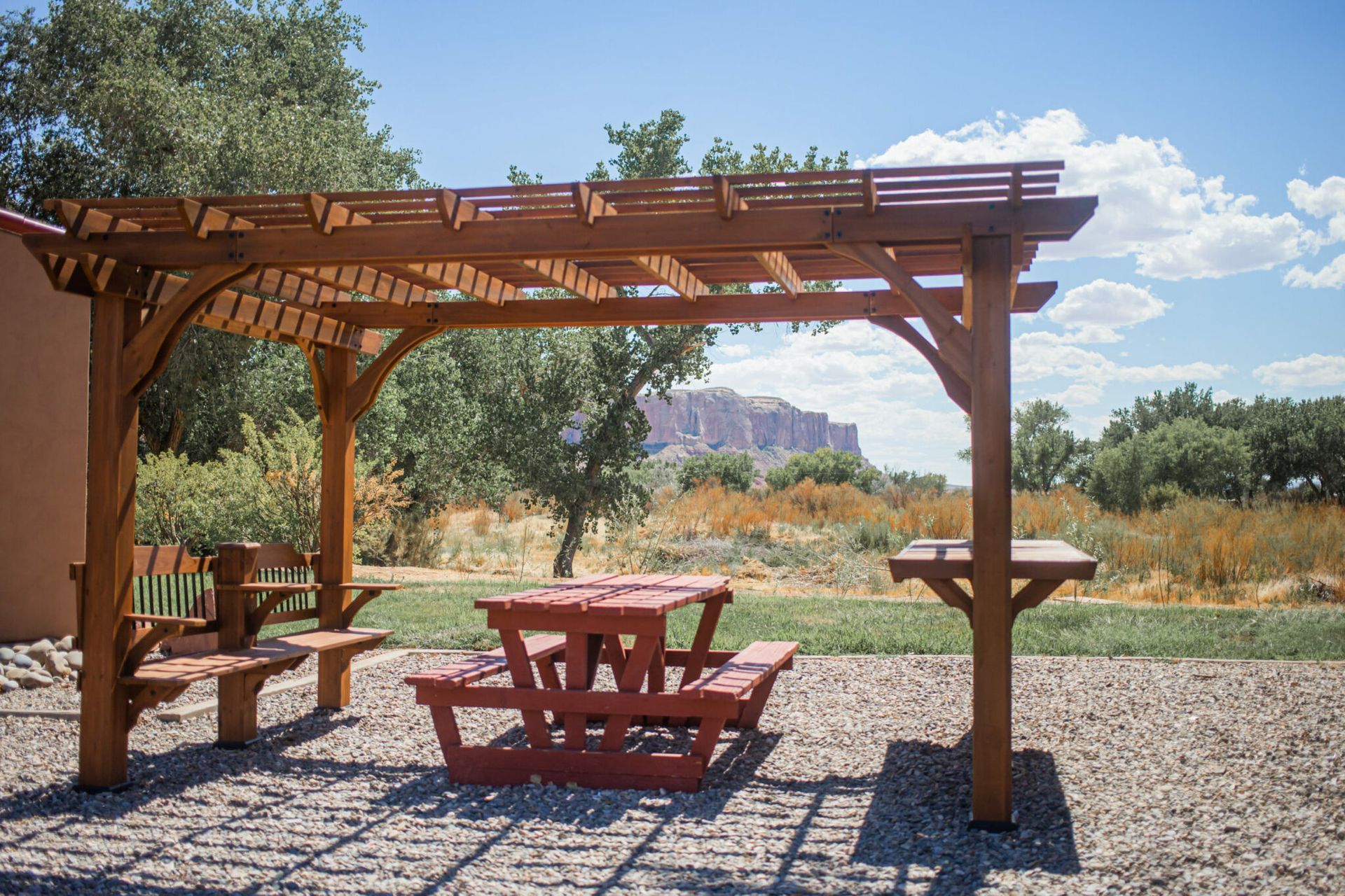Wooden picnic shelter with red table and benches in a desert landscape under a blue sky