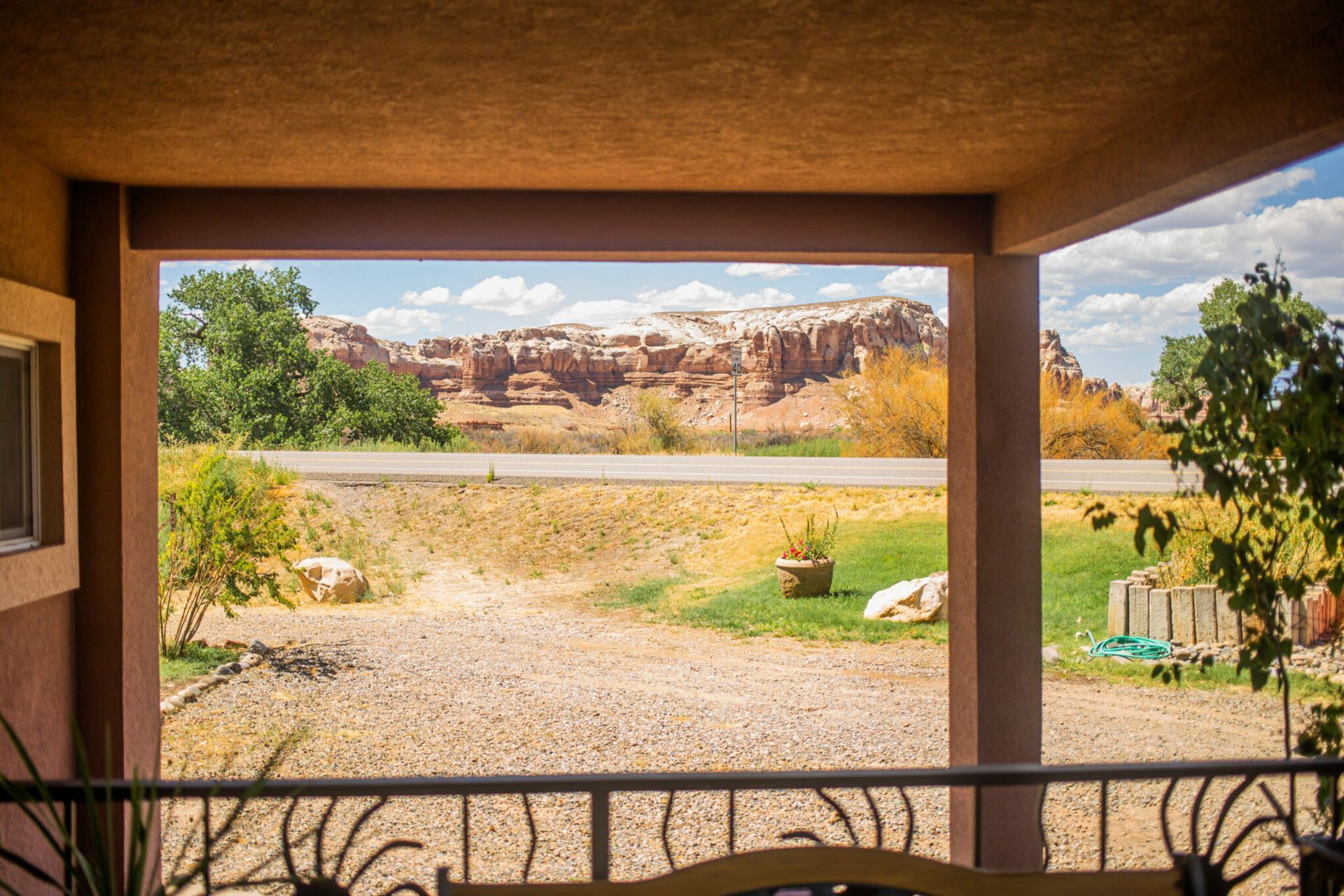 Covered patio overlooking a desert landscape with red rock cliffs, gravel yard, and green shrubs