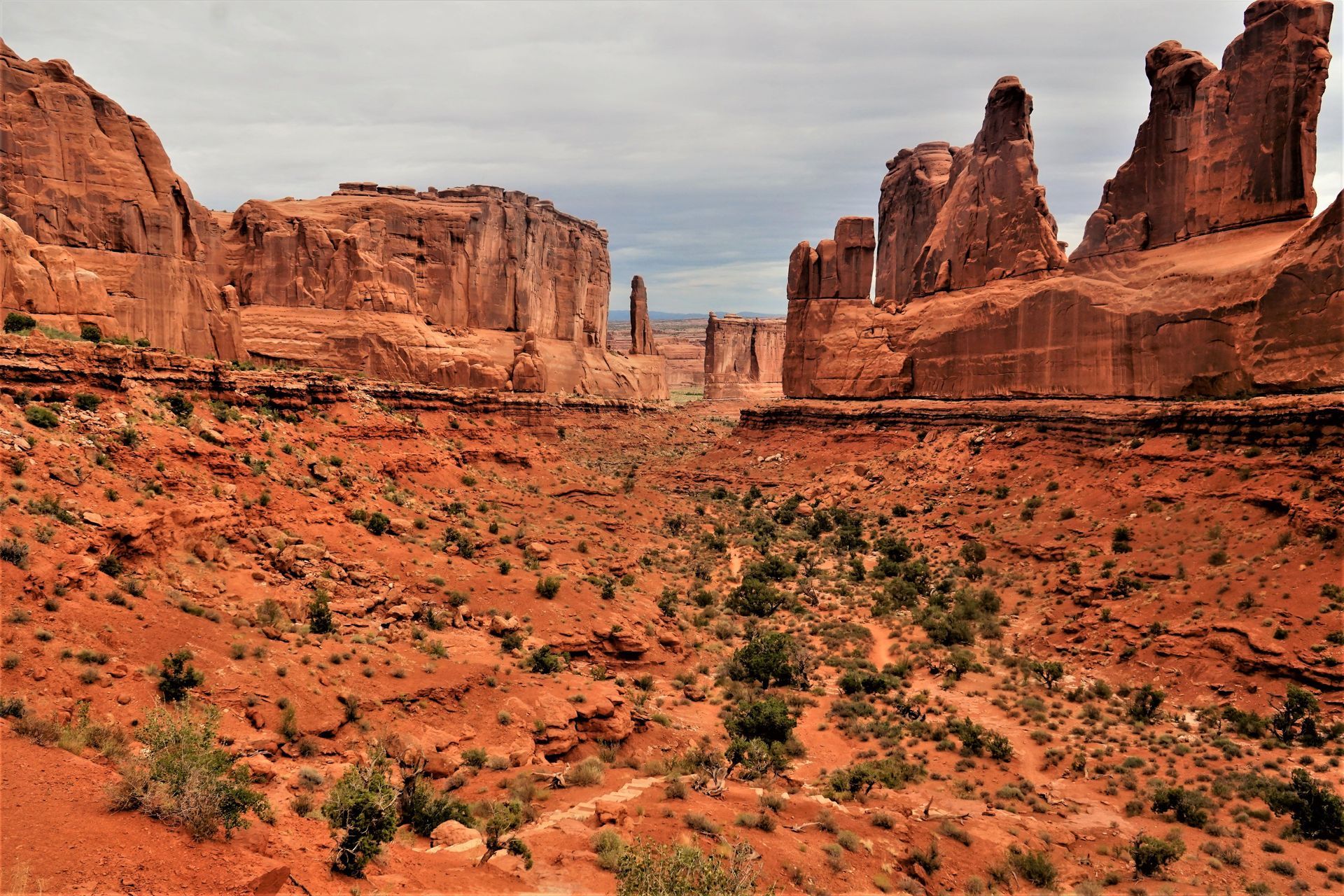 Red rock desert canyon with towering sandstone cliffs under a cloudy sky