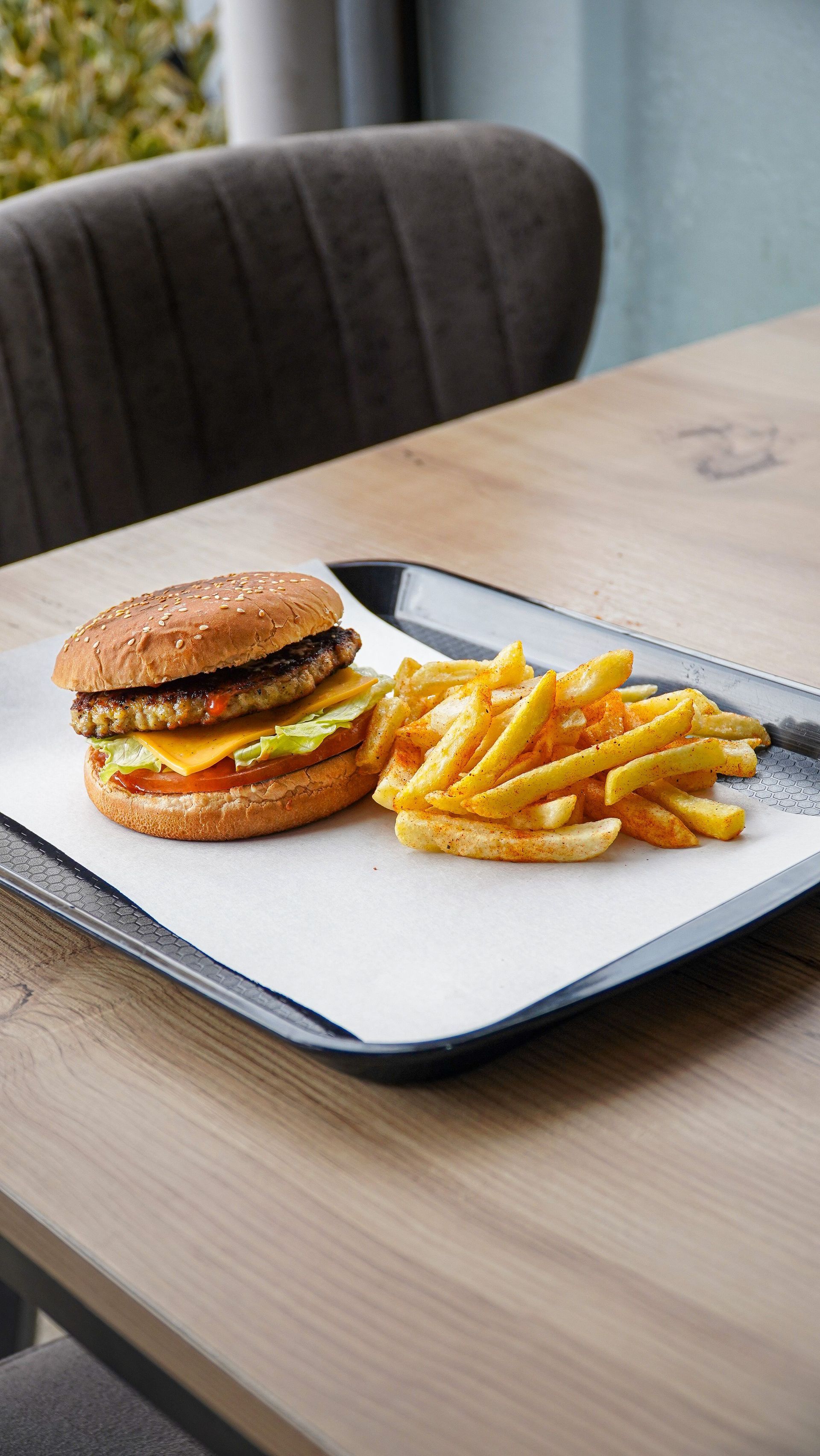 Burger and fries on a black tray on a wooden table with a chair in the background