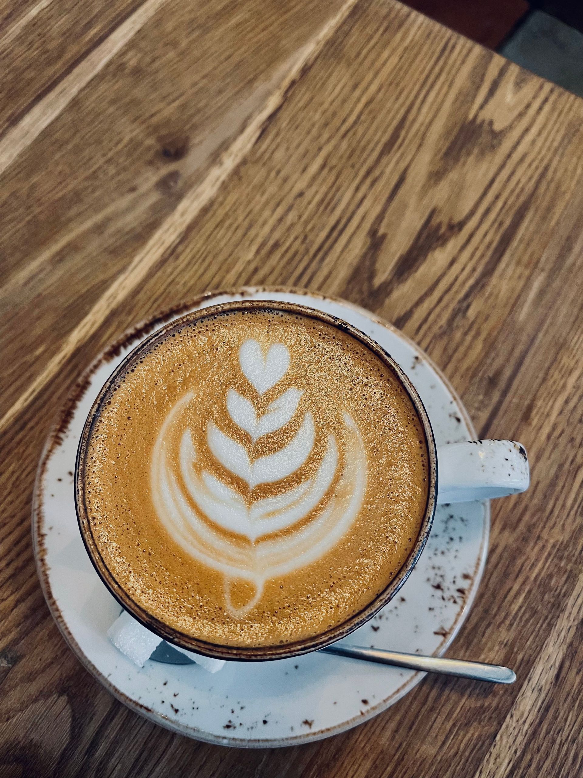 Latte with heart-shaped foam art in a white cup on a saucer, on a wooden table