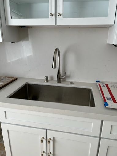 A kitchen sink with a stainless steel faucet and white cabinets.