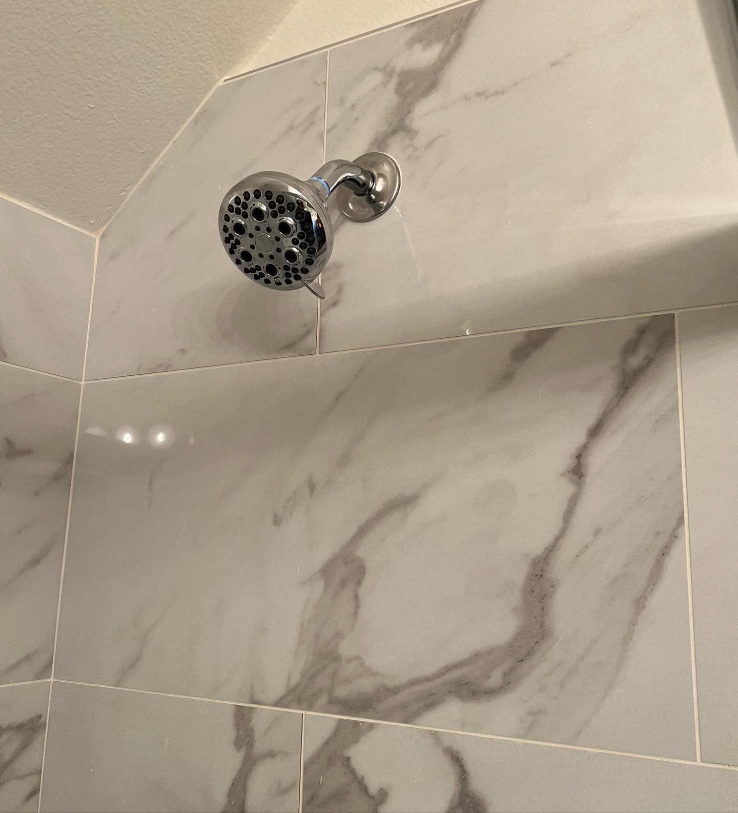A shower head is hanging from the ceiling in a bathroom with marble tiles.