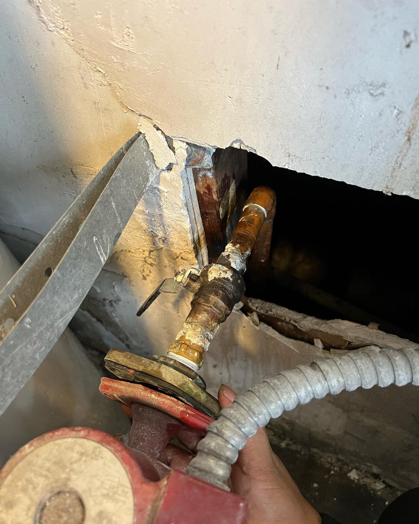A person is fixing a broken pipe in a wall.