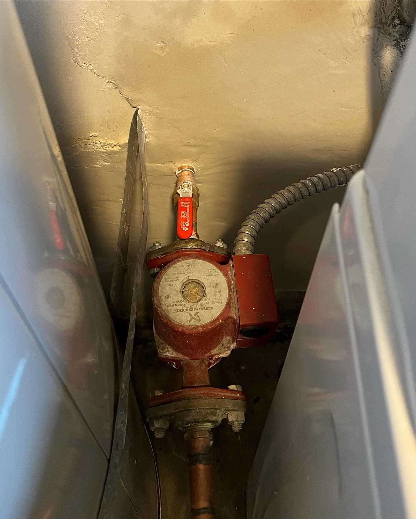 A red valve is sitting next to a white washing machine in a laundry room.
