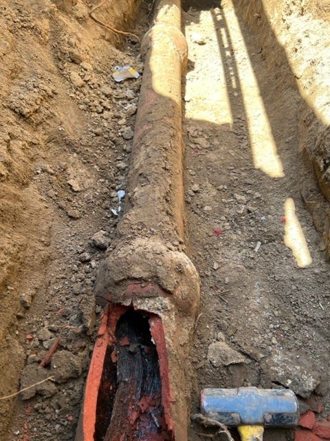 A hammer is sitting next to a pipe in the dirt.