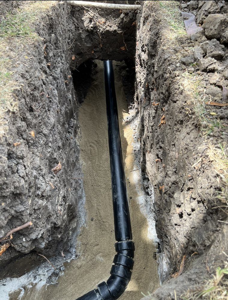 A black pipe is being installed in a hole in the ground.