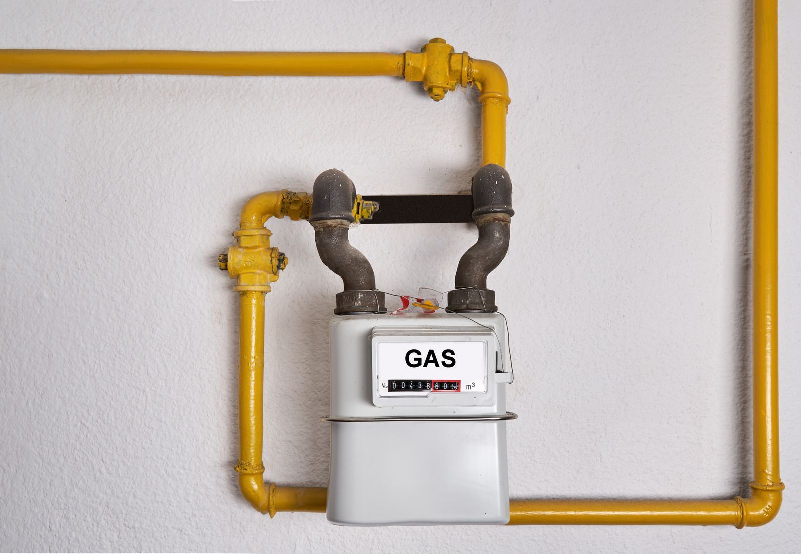 Gas meter with yellow pipes mounted on a white wall