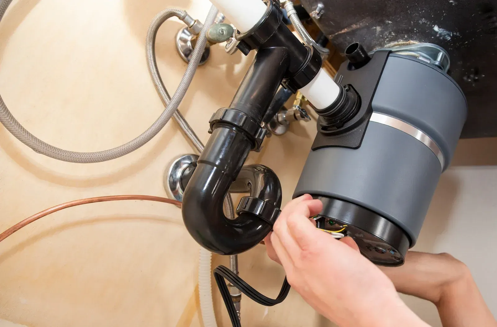 A person is fixing a garbage disposal under a sink.