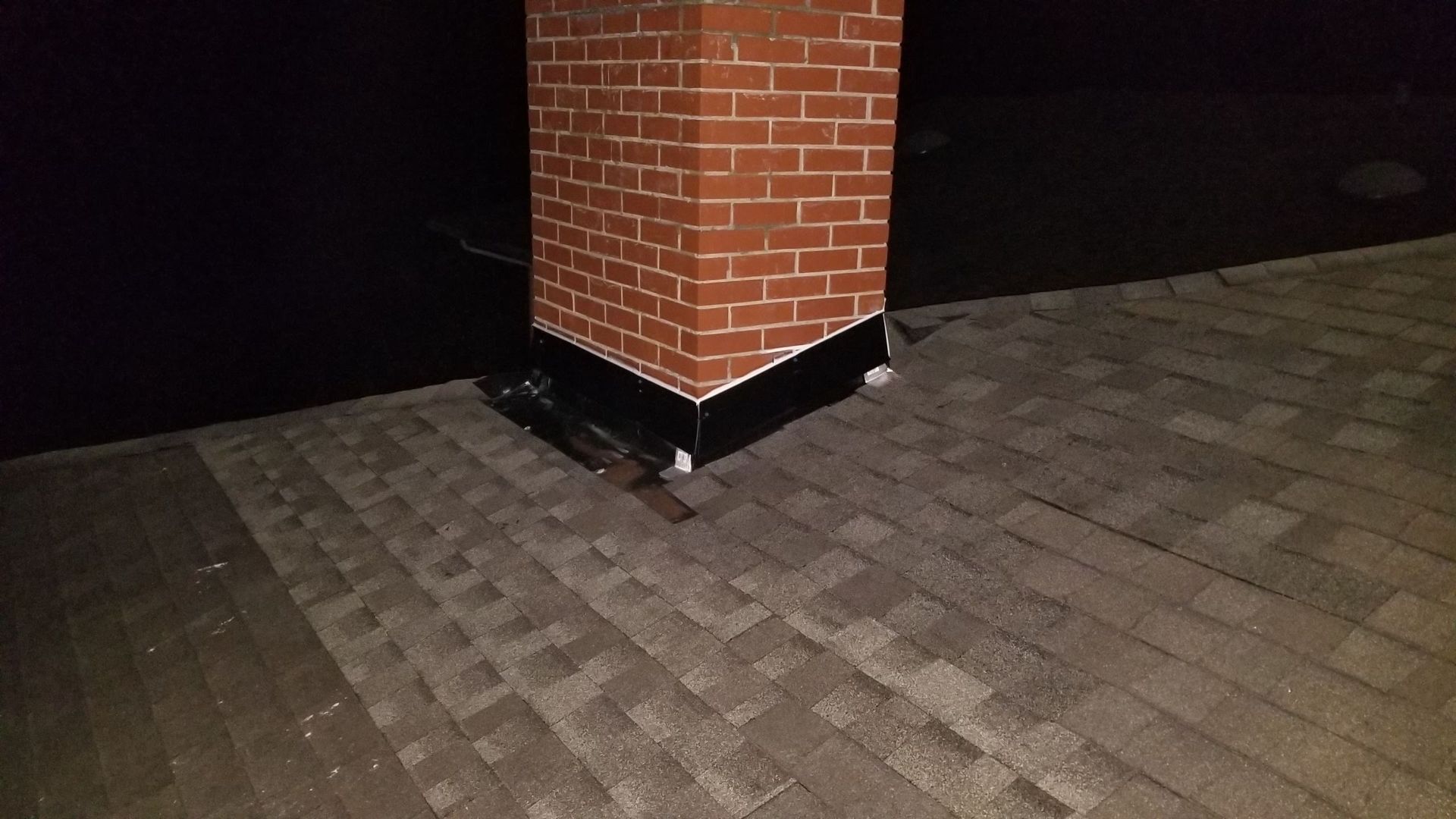 A brick chimney is sitting on top of a roof at night.