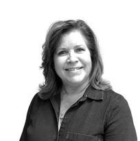 A woman in a denim shirt is smiling in a black and white photo.