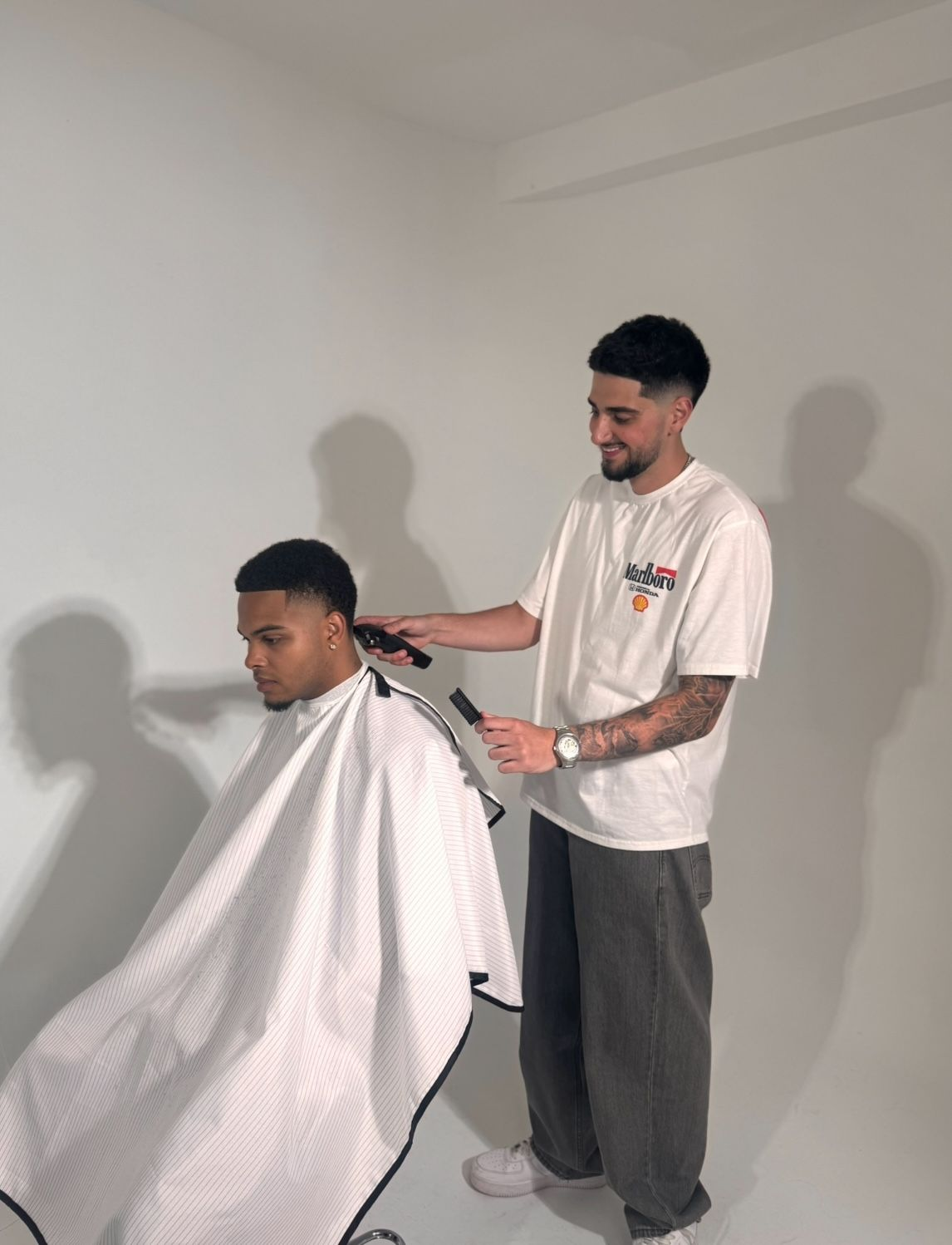Barber giving a client a haircut. The barber is using clippers in a studio with a white background.