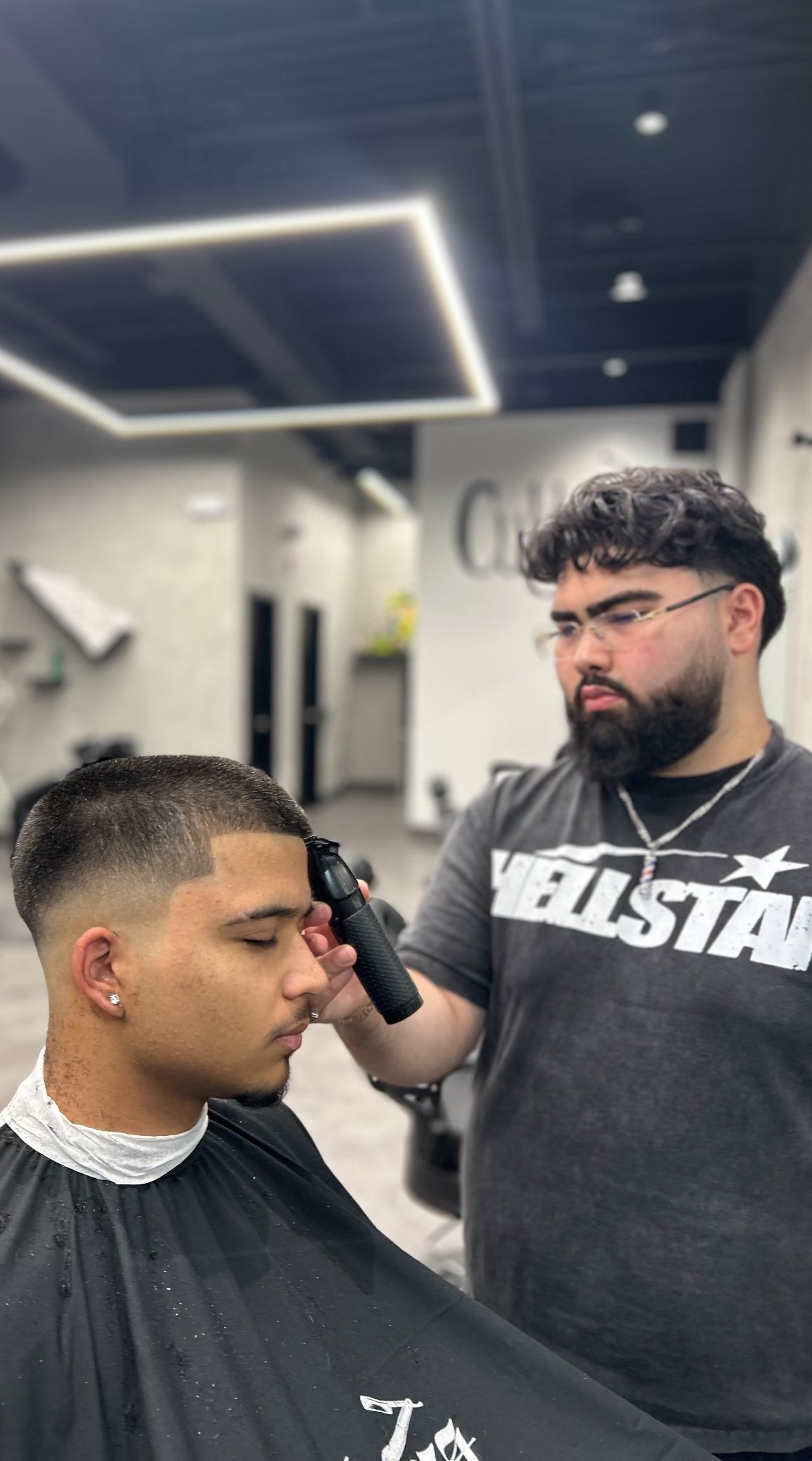 Barber giving a client a haircut. The barber is using clippers. Interior of a barber shop.