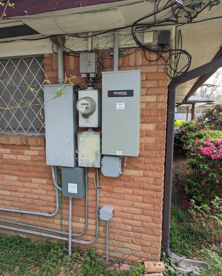 Brick wall with electric meter, breaker boxes, and overhead utility wires beside a house.