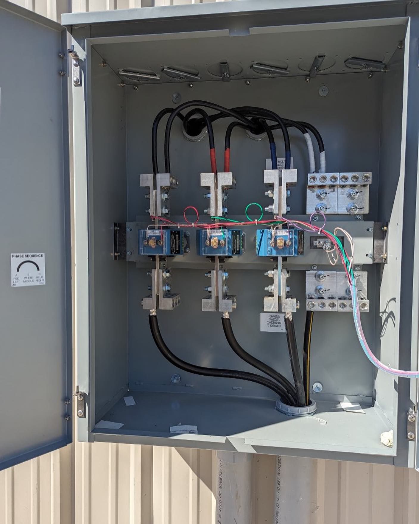 Open electrical control panel with wiring, relays, and circuit breakers in a gray cabinet