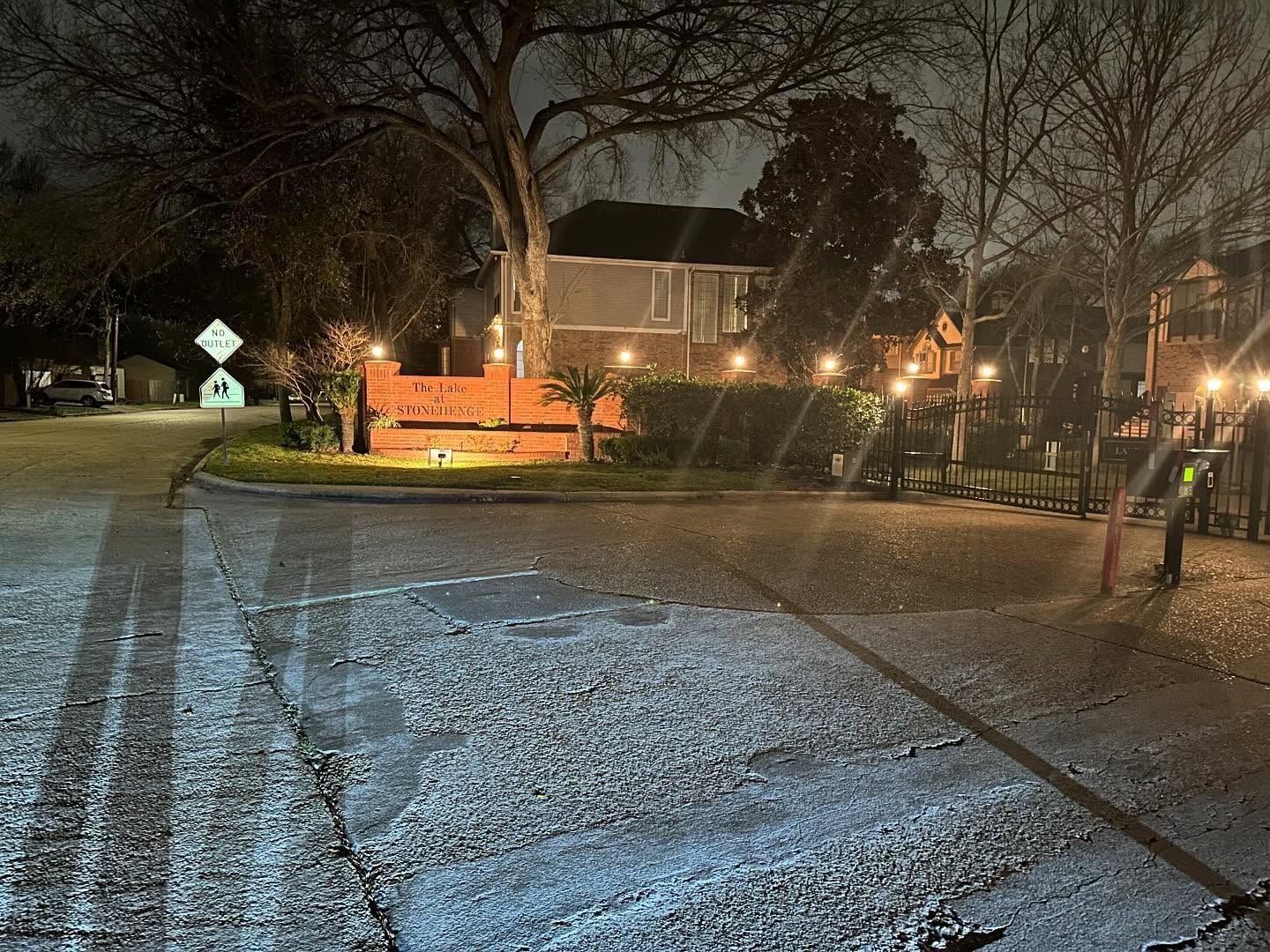 Snow-covered park path at night with glowing streetlights and a lit bench near bare trees