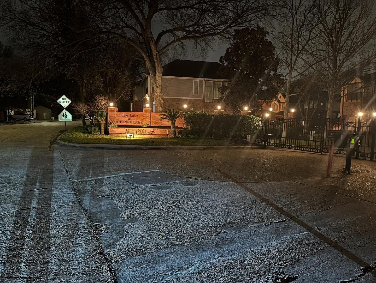 Snow-dusted park path at night with glowing streetlights and bare trees