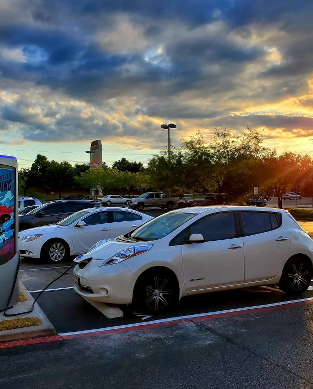 White hatchback in a parking lot at sunset with dramatic cloudy sky and other cars nearby