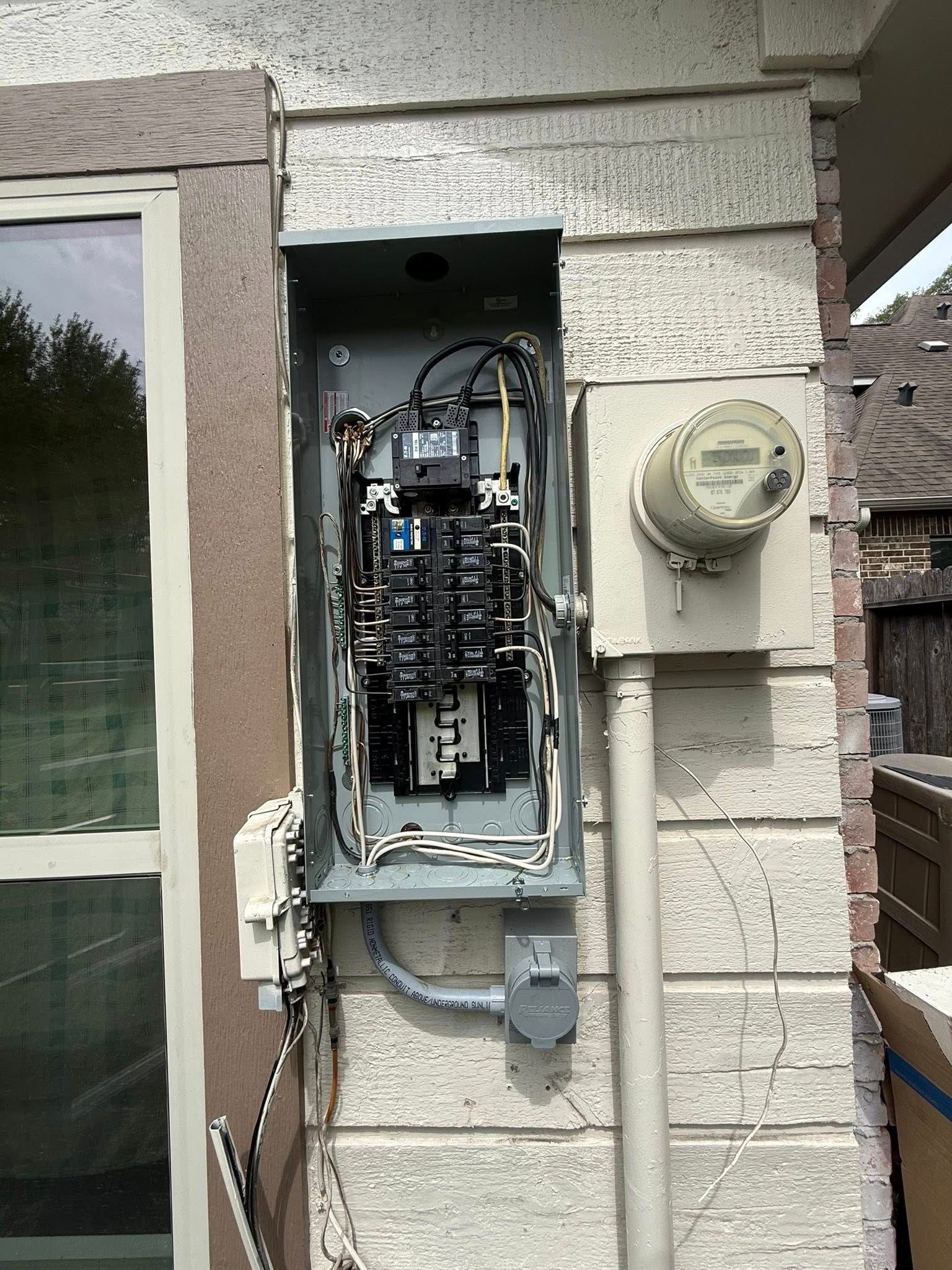 Open electrical breaker panel mounted on an exterior wall next to a utility meter.