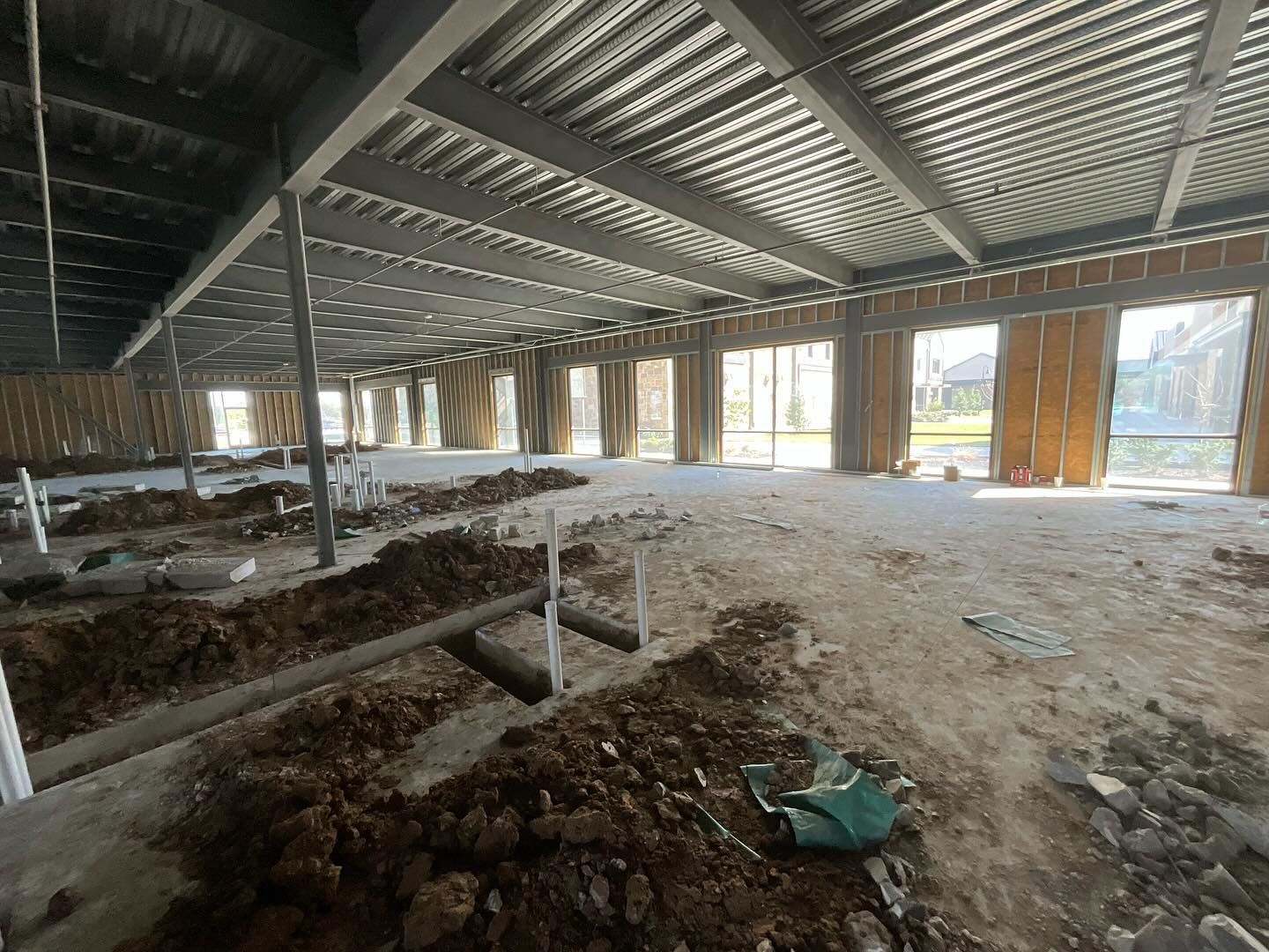 Interior of an unfinished building with exposed steel beams, dirt floor, and daylight through open walls