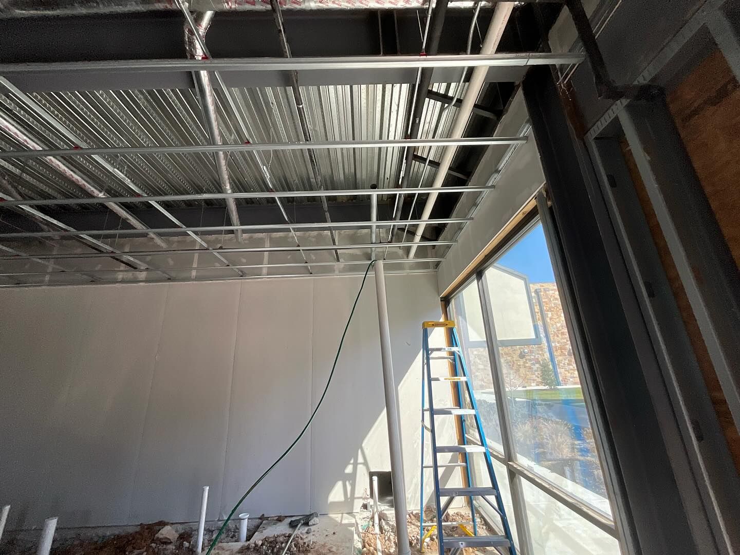 Interior under construction with metal ceiling framing, ladder, and large window wall