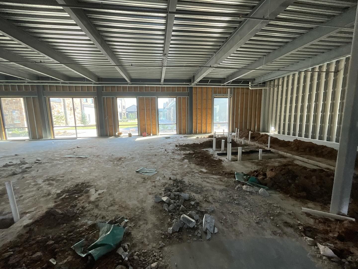 Interior of an unfinished building with steel framing, exposed walls, concrete floor, and construction debris