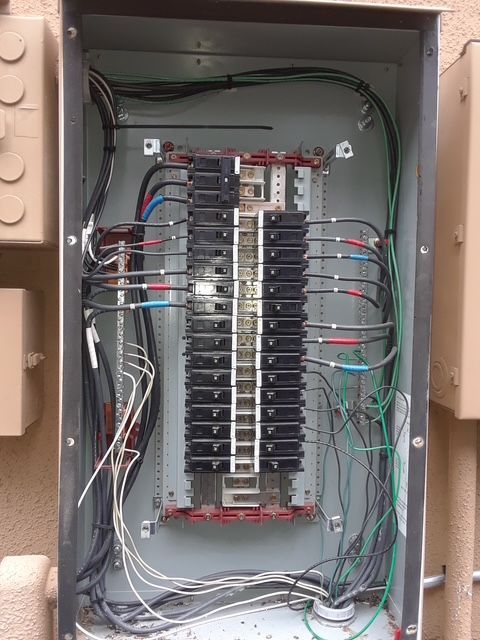 Open electrical breaker panel with wiring and circuit breakers inside a beige metal box