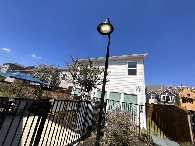 Residential backyard with a black fence, white house, and tilted streetlamp under a clear blue sky