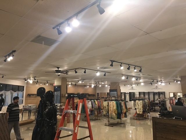 Clothing store interior with racks of colorful clothes, ladder, and ceiling track lights
