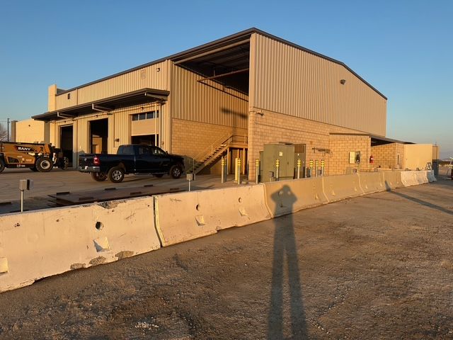 Industrial warehouse exterior with parked truck and concrete barriers in warm sunlight