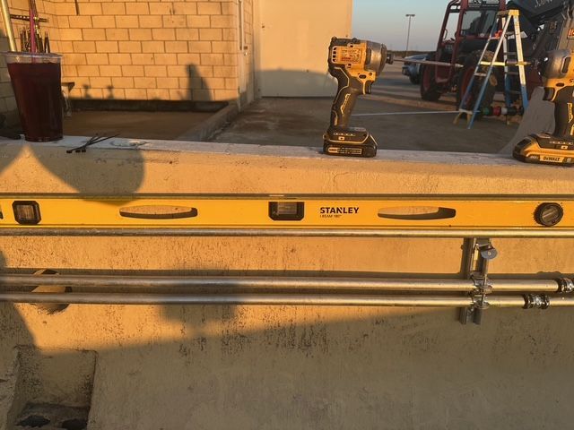 Construction tools and yellow spirit level on a wall-mounted pipe in a sunlit work area