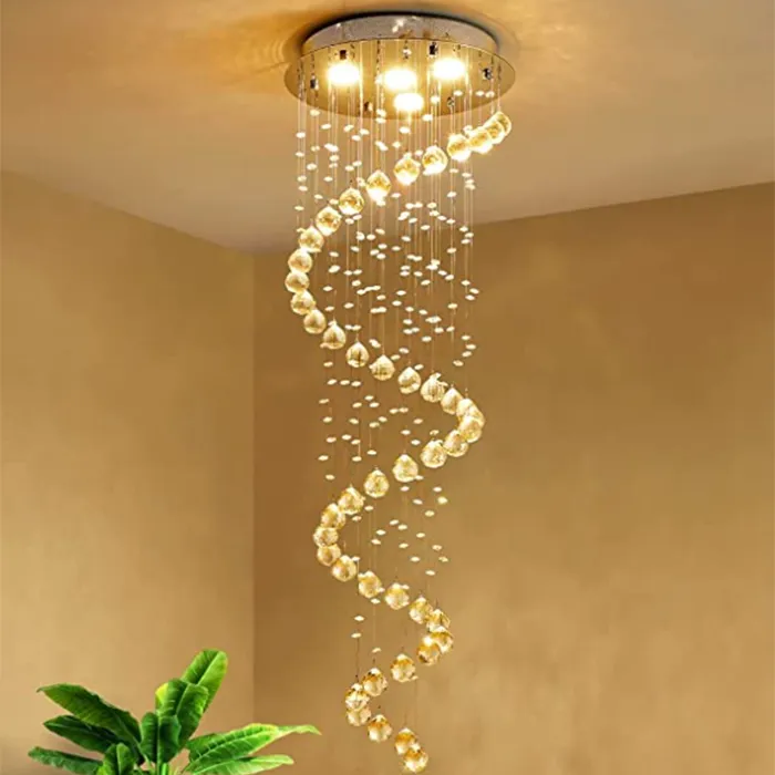 Gold spiral chandelier hanging from a ceiling in a beige room, with green plant leaves below