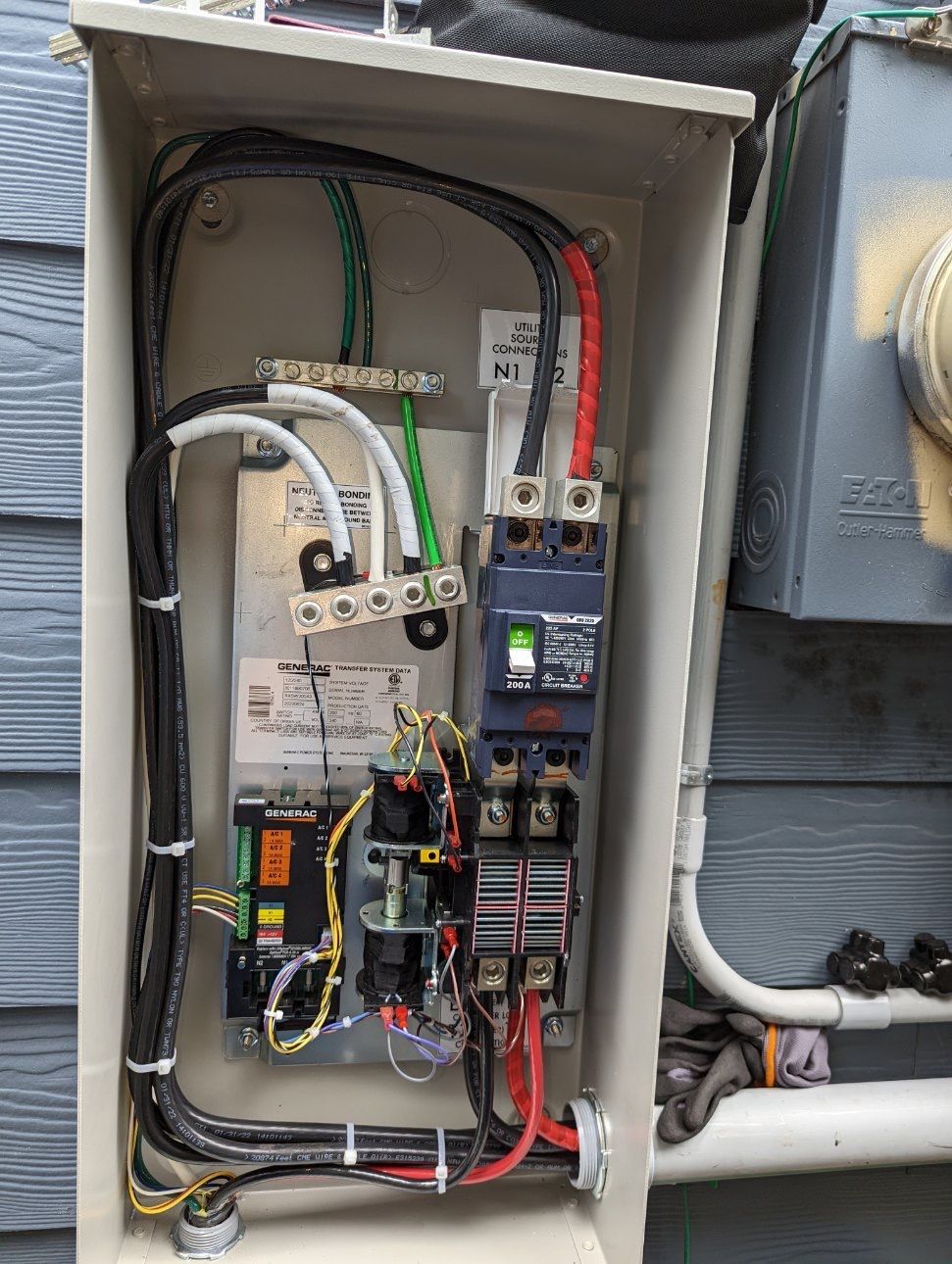 Open electrical service panel with wires, breakers, and conduit mounted on an exterior wall.