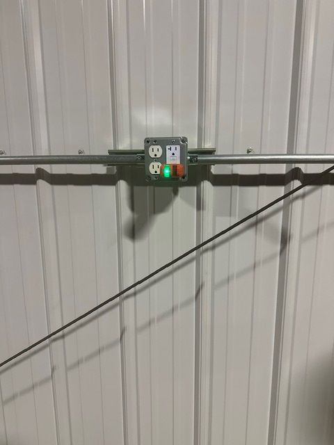 Electrical outlet box mounted on a corrugated metal wall with a diagonal pipe and cable shadow