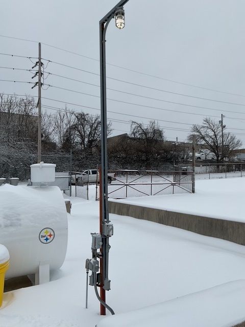 Snow-covered outdoor utility equipment beside a metal gate and lamp post in a winter yard