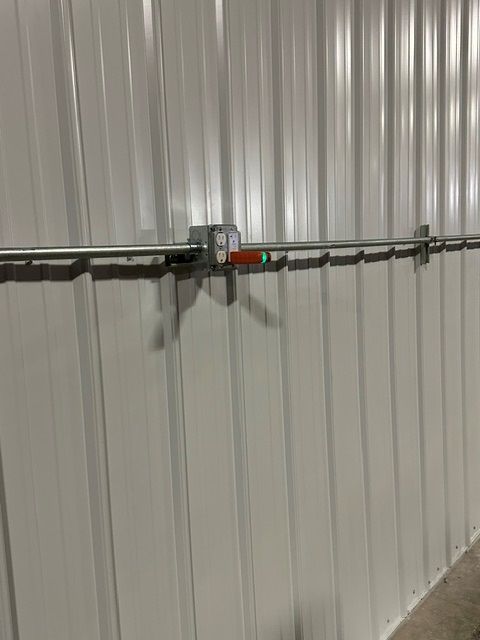 Metal conduit pipe with red valve mounted across a corrugated wall in an industrial interior