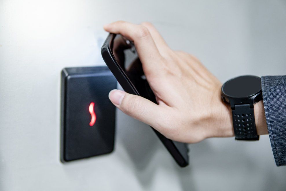 Hand with a black phone near a security access panel, activating it. The person wears a smartwatch.