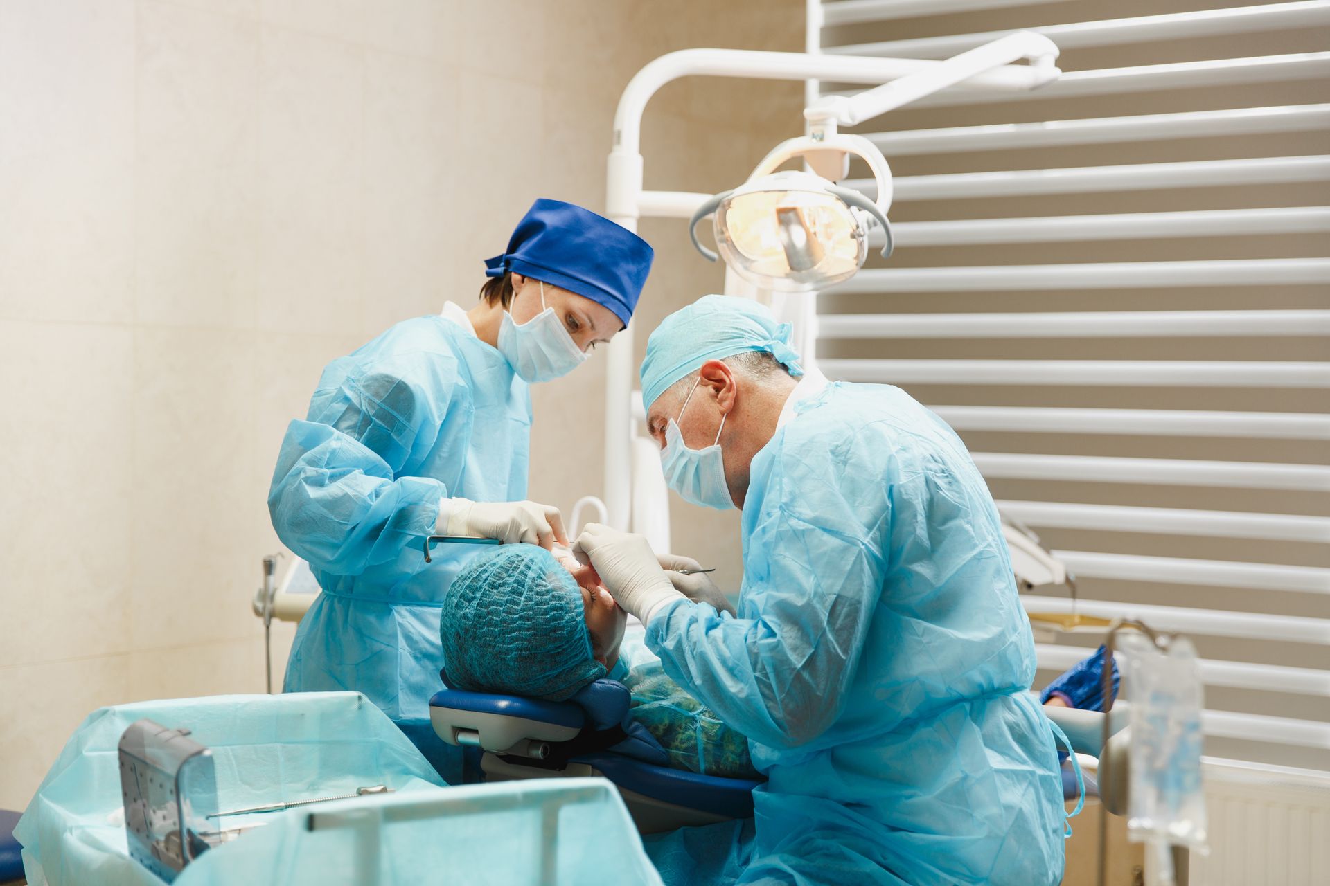 Two dentists in blue scrubs work on a patient in a dental clinic operating room.